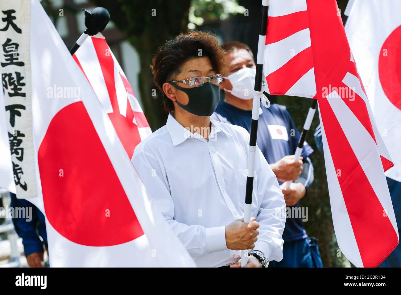 Tokyo, Japan. 15th Aug, 2020. Japanese nationalists wearing face masks hold war flags of the Imperial Japanese Army during the 75th anniversary of Japan's surrender in World War II at Yasukuni Shrine. This year, the temple has set signboards promoting the social distancing to prevent the spreading of the new coronavirus (COVID-19) disease at the Yasukuni Shrine. Credit: Rodrigo Reyes Marin/ZUMA Wire/Alamy Live News Stock Photo
