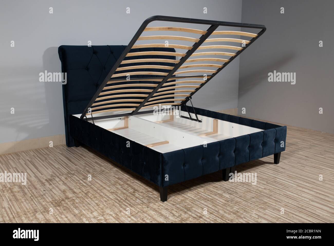 Bed with blue upholstery without mattress in an empty room and opened