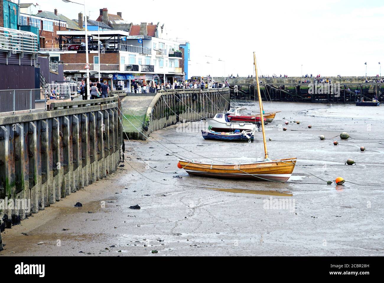 Bridligton, Yorkshire, UK. August 05, 2020. Holidaymakers throng the harbor quay at low tide with boats moored on sand at Bridlington in Yorkshire, UK Stock Photo