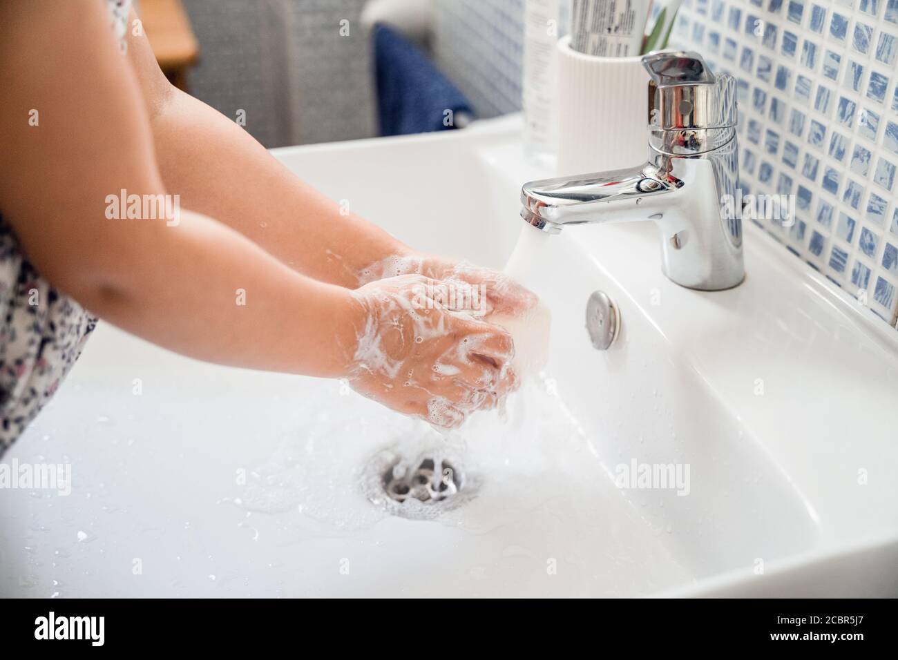 Little girl washes hands with bar of soap in washbasin under running tap water Stock Photo
