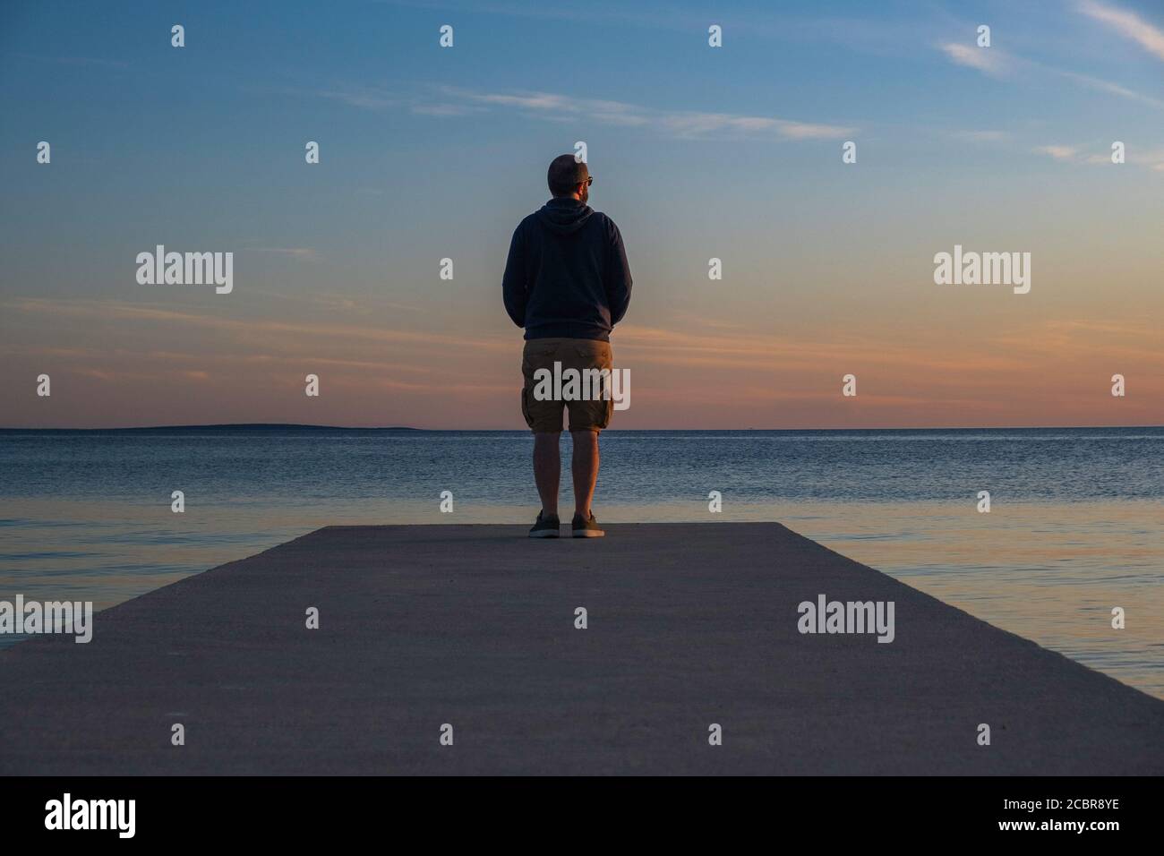 Man standing on long dock and watching sea horizon in sunset, island od Pag, Adriatic sea, Croatia, thoughtfulness concept Stock Photo