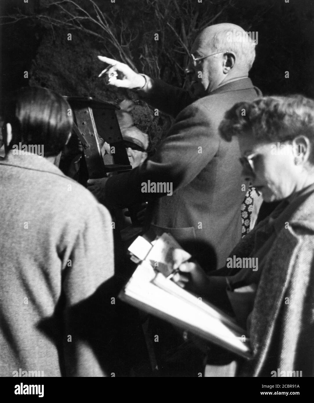 CECIL B. DeMILLE on set candid with Cinematographer GEORGE BARNES (back to camera at left) and Script Supervisor CLAIRE BEHNKE during filming of SAMSON AND DELILAH 1949 director CECIL B. DeMILLE Paramount Pictures Stock Photo