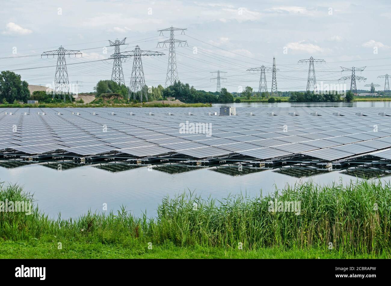 Zwolle, The Netherlands, July 19, 2020: a large array of solar panels reflects in the artificial lake Sekdoorne Plas, with electricity pylons and powe Stock Photo
