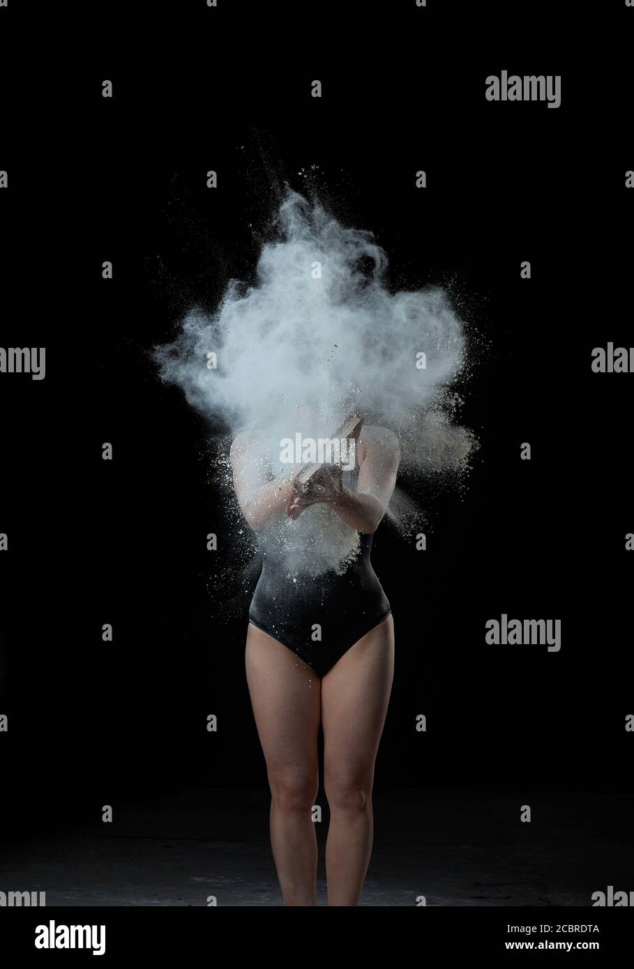 young beautiful woman in a black textile bodysuit holds a book in her hands, cloud of white wheat flour flies out of the book in different directions, Stock Photo