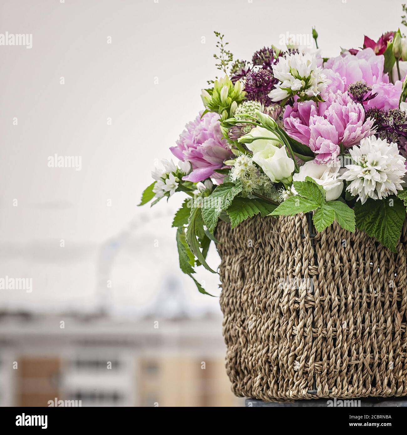 Bouquet of flowers in a basket on a gray background. Peonies, eustoma, raspberry leaves. Copy space Stock Photo