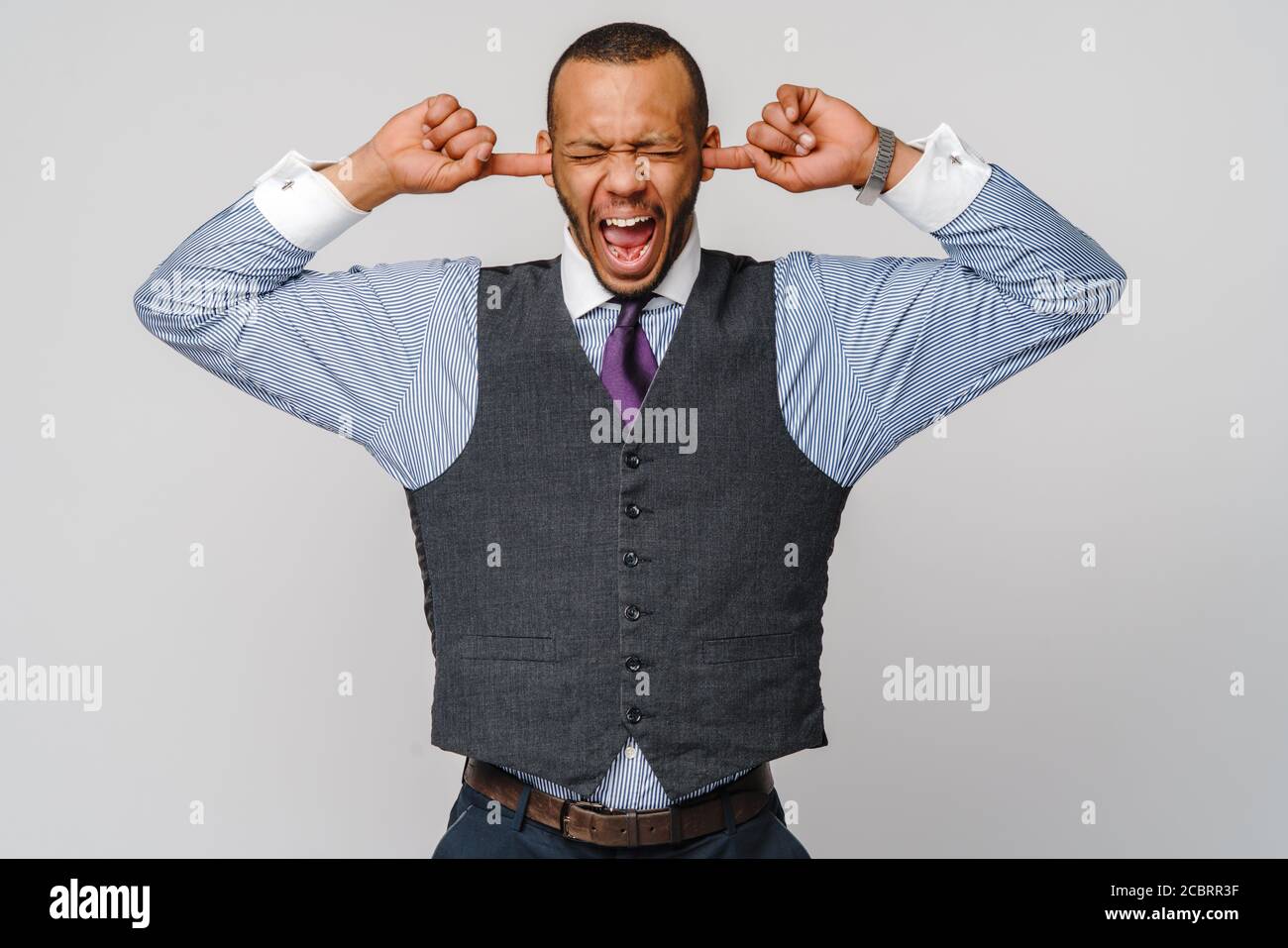 Young african american man holding his hands up to his ears trying to mute all the voices he hears and screaming Stock Photo