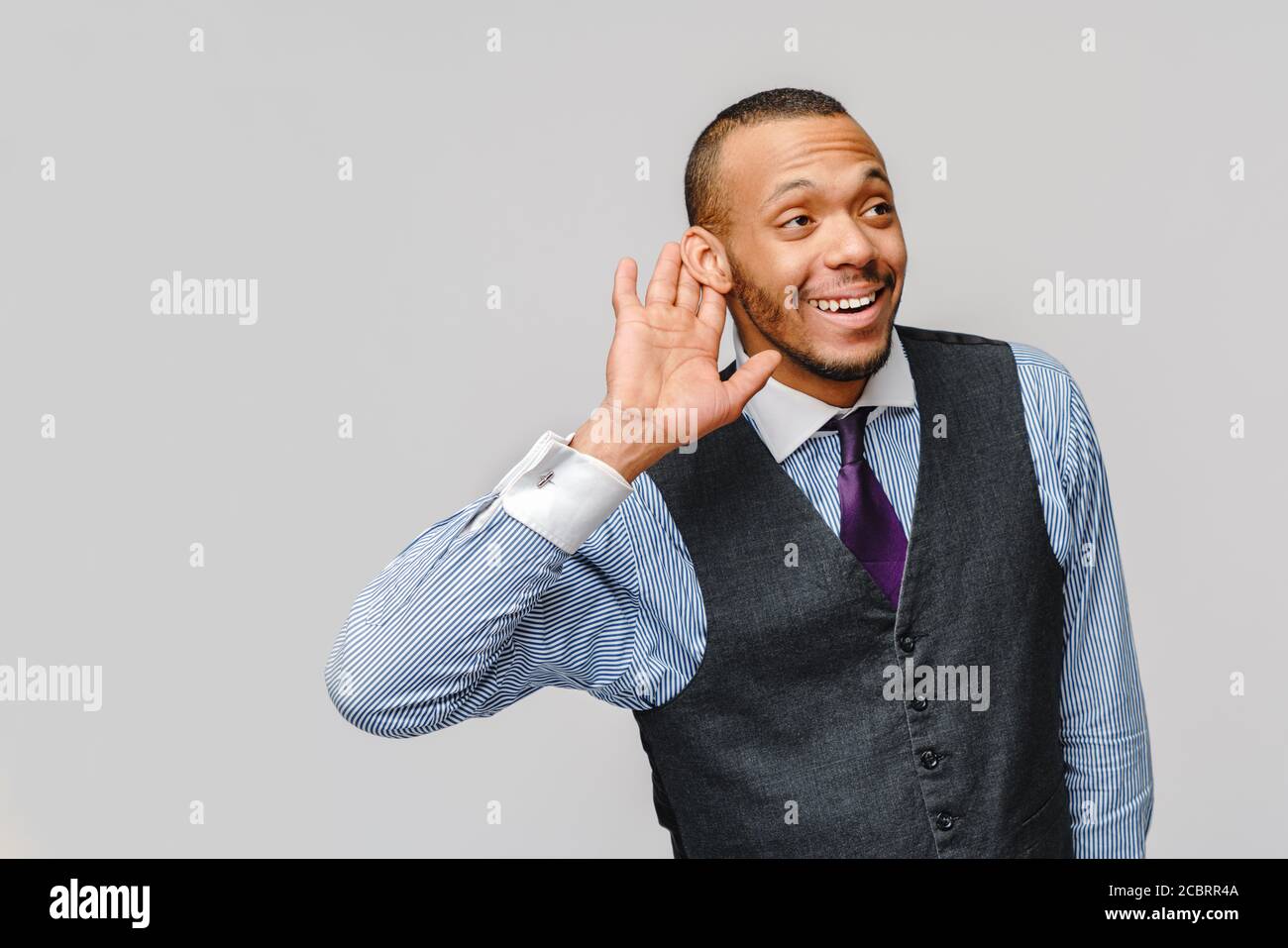 Young handsome African American businessman listening something or eavesdropping, can't hear you concept over grey background Stock Photo