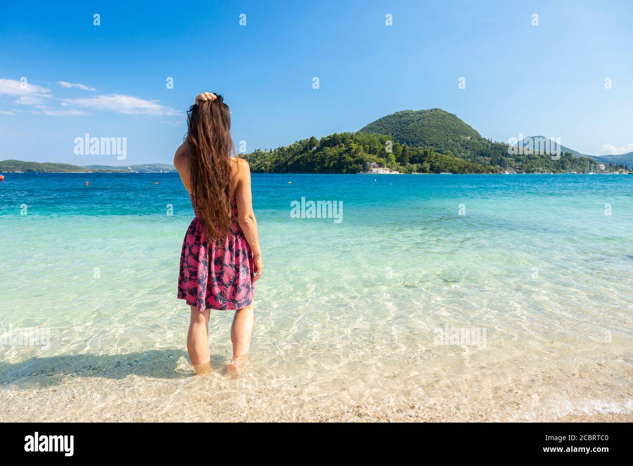 A woman wades in shallow clear water at Nidri Beach, Lefkada, Ionian Islands Greece Stock Photo