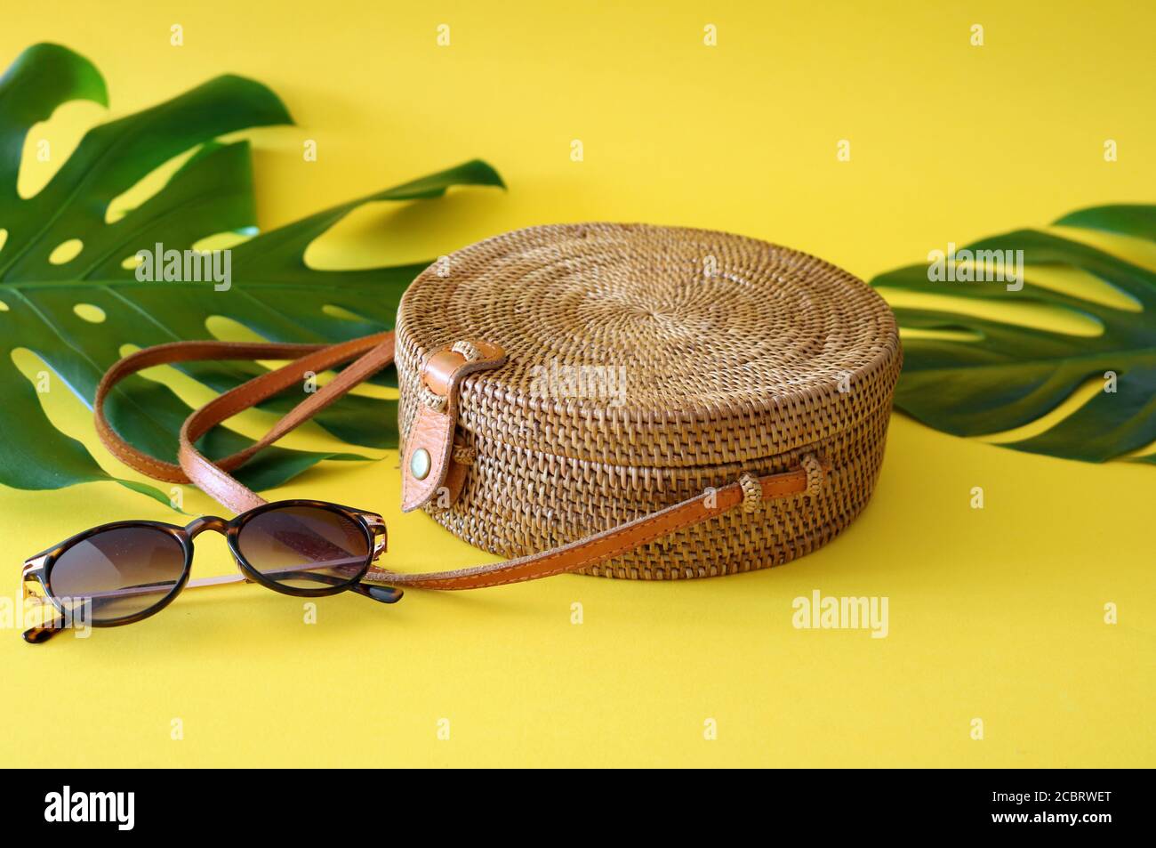 Handwoven Boho Bali Round Ata Rattan Beach Bag With Button Clip on a yellow and turquoise background Stock Photo