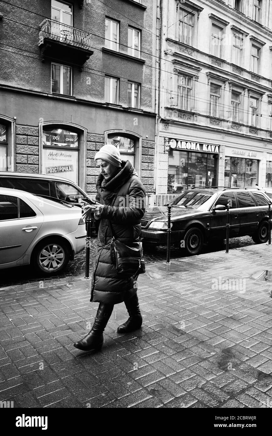Walking with smartphone. Lviv/Ukraine - January 30, 2020: Woman walking on the Akademika Hnatyuka street without looking up from her smartphone Stock Photo