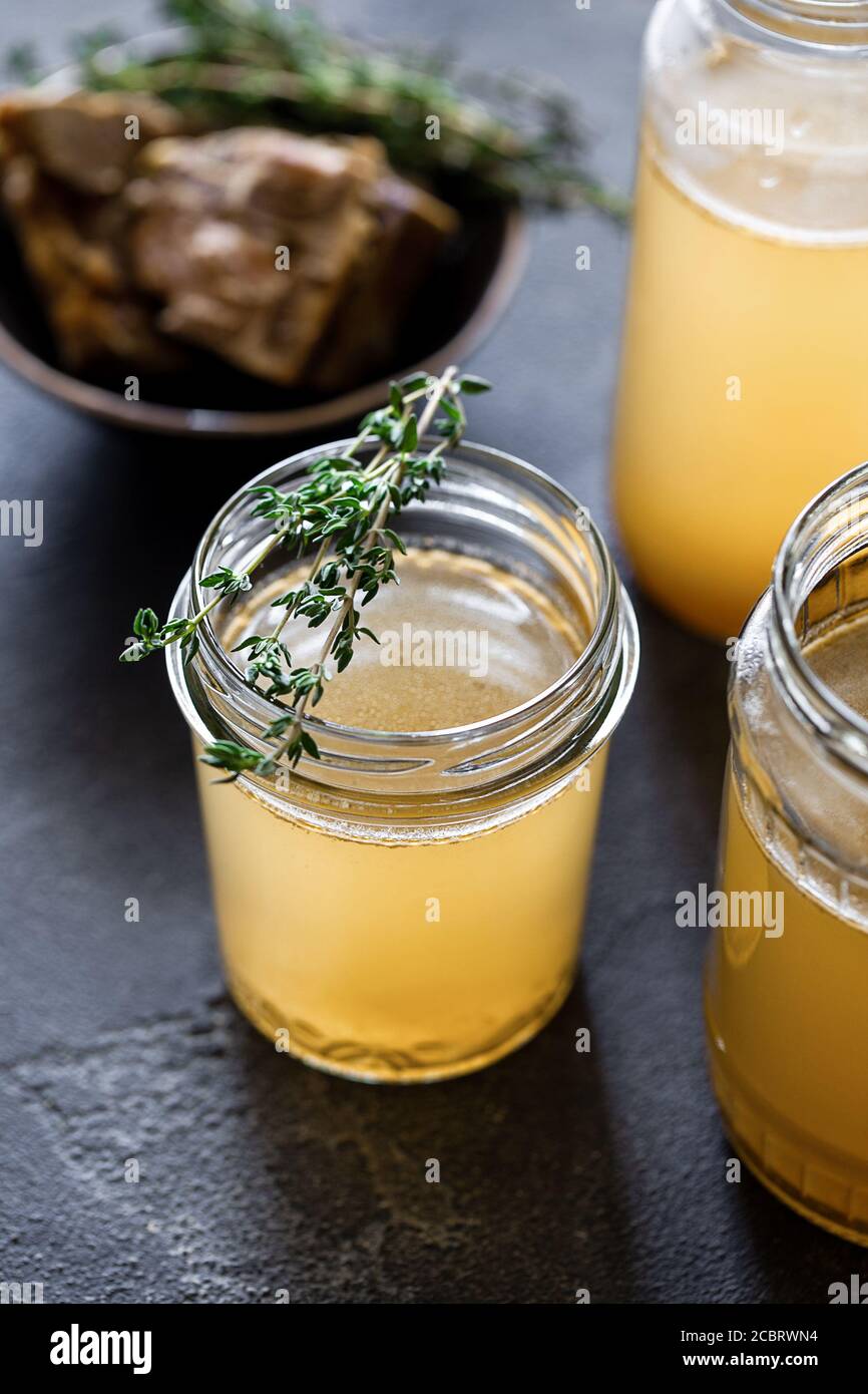 Glass jar with yellow fresh bone broth on dark gray background. Healthy