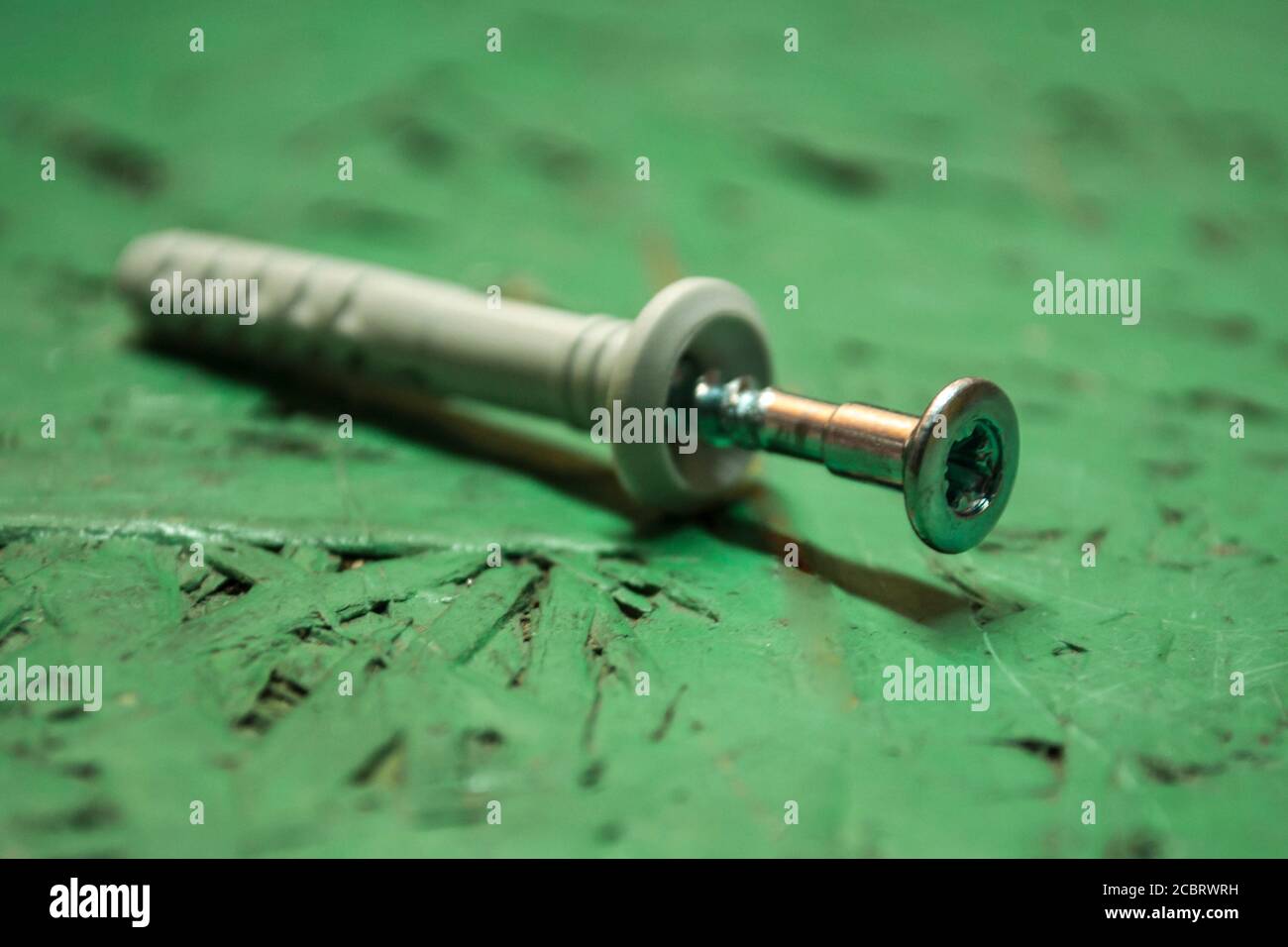 One metal screw connected to a plastic dowel on a green background. Focus on the screw Stock
