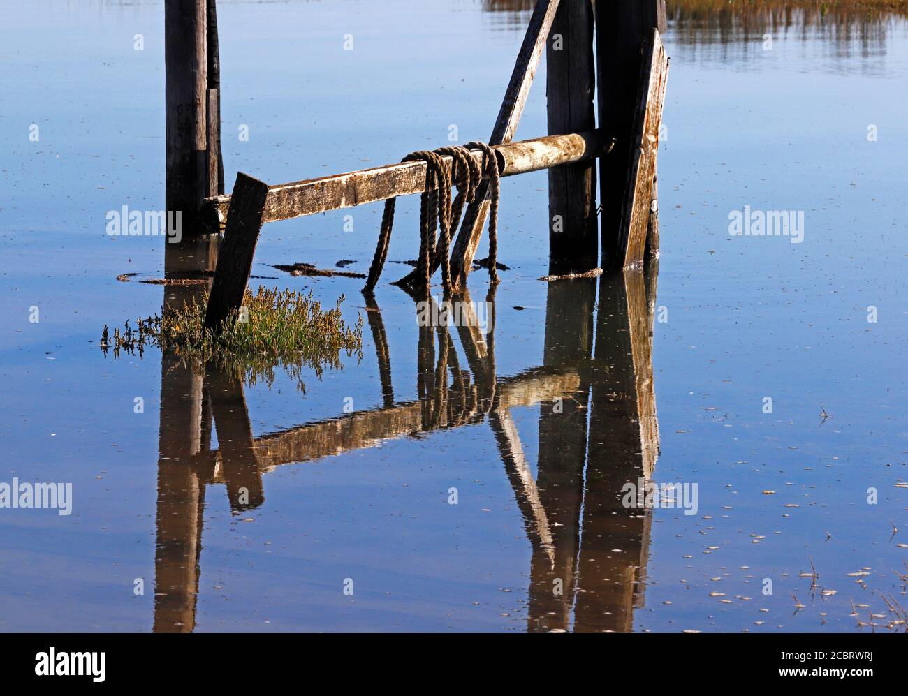 A symmetrical composition of wooden staging and ropes reflecting in overtopping flood tide at the harbour at Thornham, Norfolk, England, UK. Stock Photo