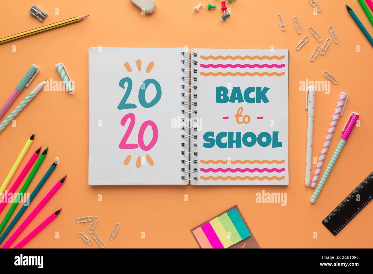 Stock photo of the back to school concept with an open notebook with lettering and some stationery objects on a salmon background Stock Photo