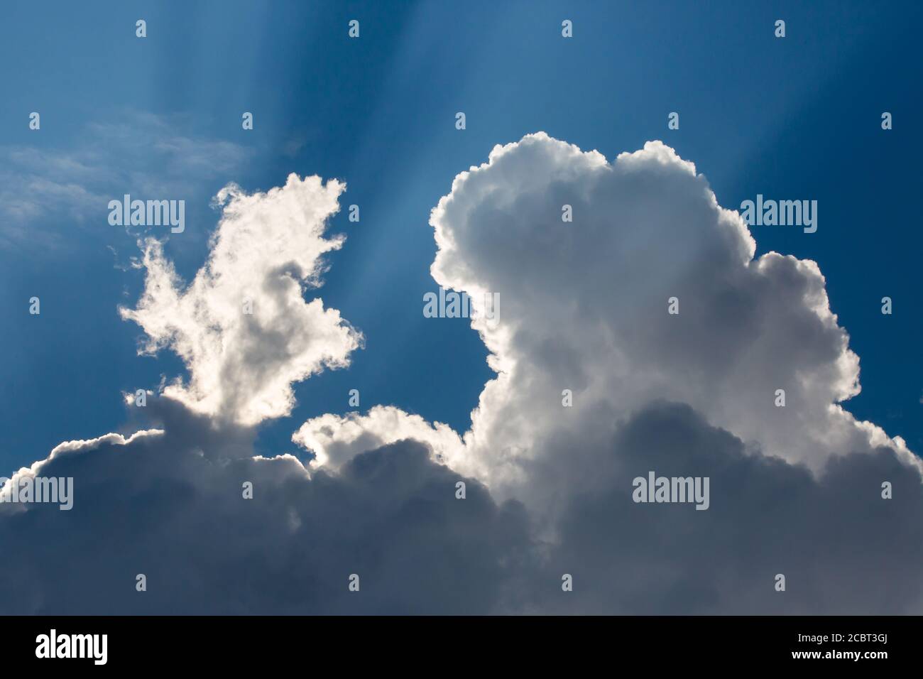 Sunbeams streak a deep blue sky behind dramatic cumulus clouds. Stock Photo