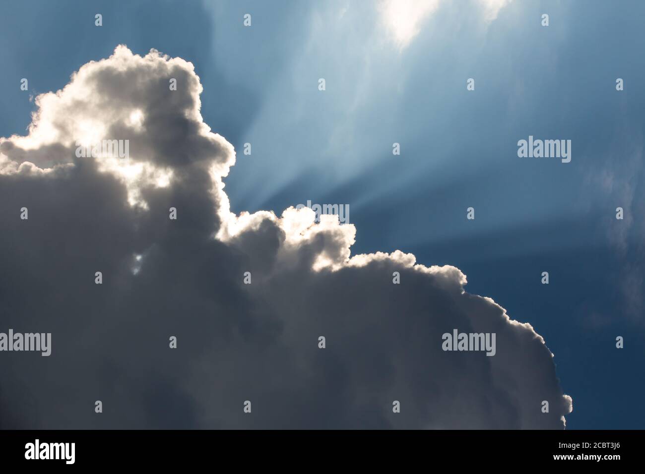 Sunbeams streak a deep blue sky behind dramatic cumulus clouds. Stock Photo