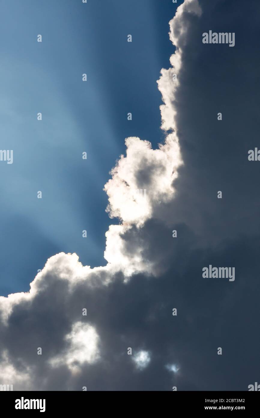 Sunbeams streak a deep blue sky behind dramatic cumulus clouds. Stock Photo