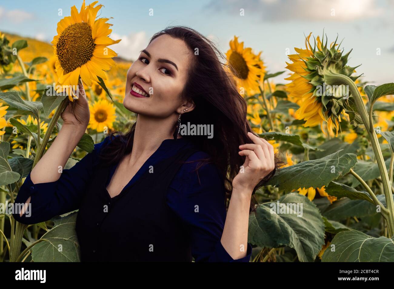 Asian girl is surrounded by sunflowers and smiling. Field with sunflowers on the background. Stock Photo