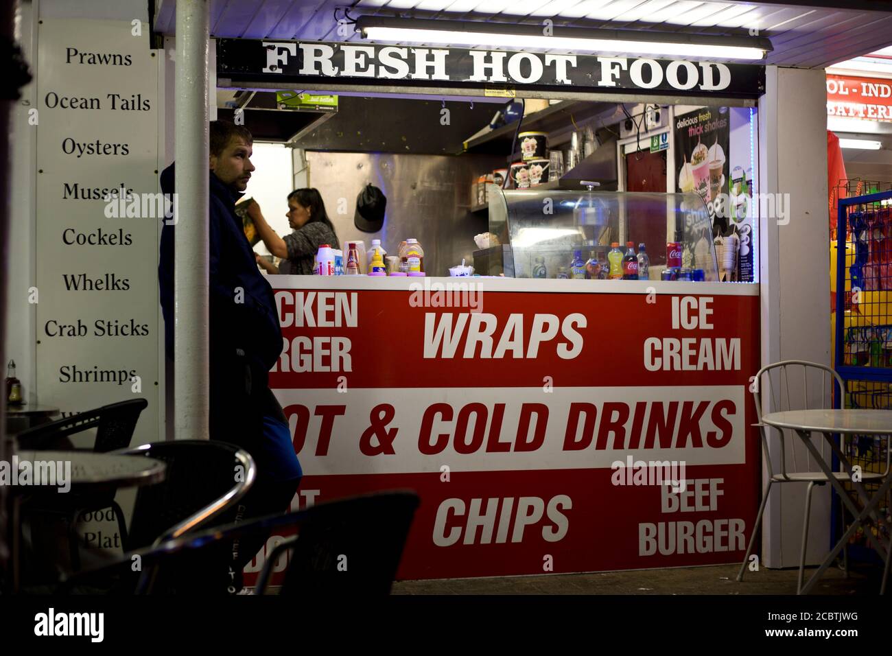 Man waiting outside a street vendor take away. Gritty scene, late night eating, fresh hot food, Blackpool promenade, quick eats, Street photography, Stock Photo