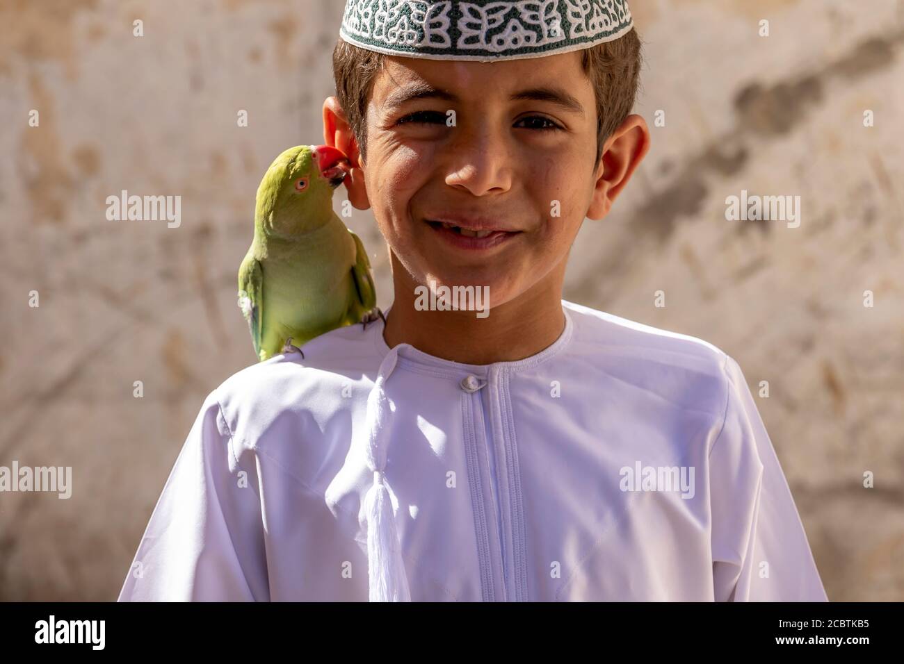 An Omani boy holding his pet parrot on his shoulder Stock Photo