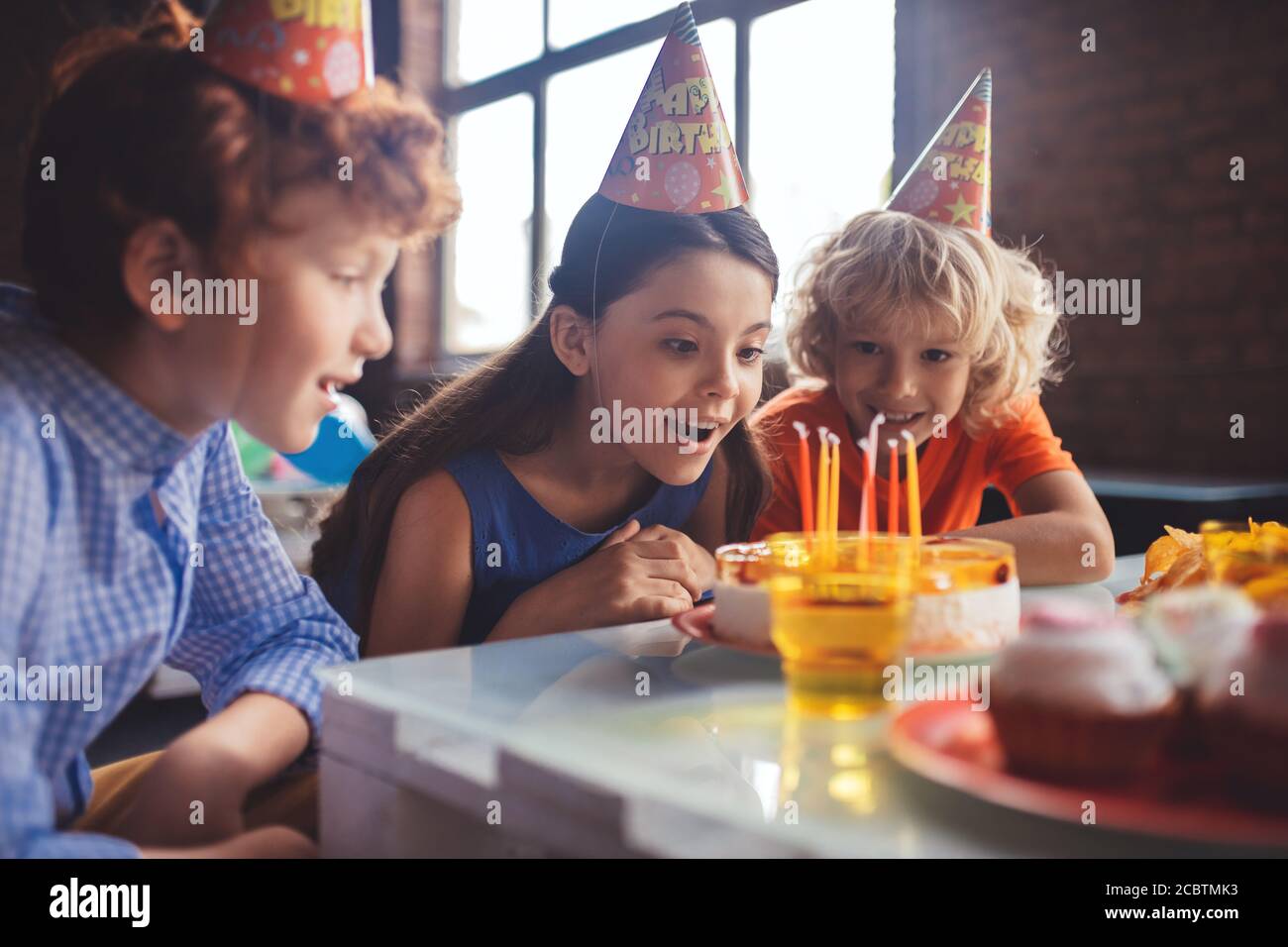 Three kids looking at the cake and feeling amused Stock Photo