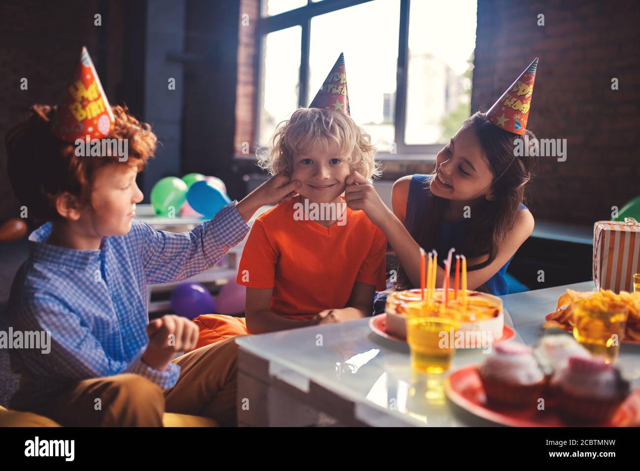 Two friends pulling cheeks of their friend and smiling Stock Photo Alamy