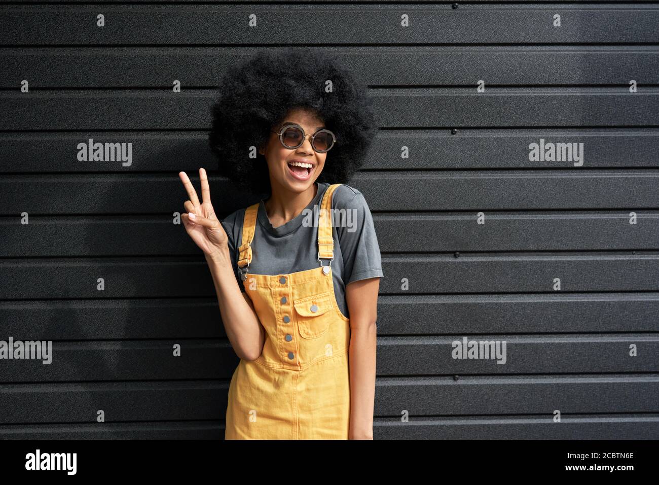 Happy African teen hipster girl wear stylish glasses stand against black wall. Stock Photo