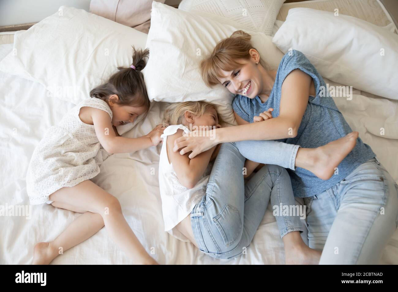 Friendly laughing mother and daughters tickling and playing on bed Stock Photo