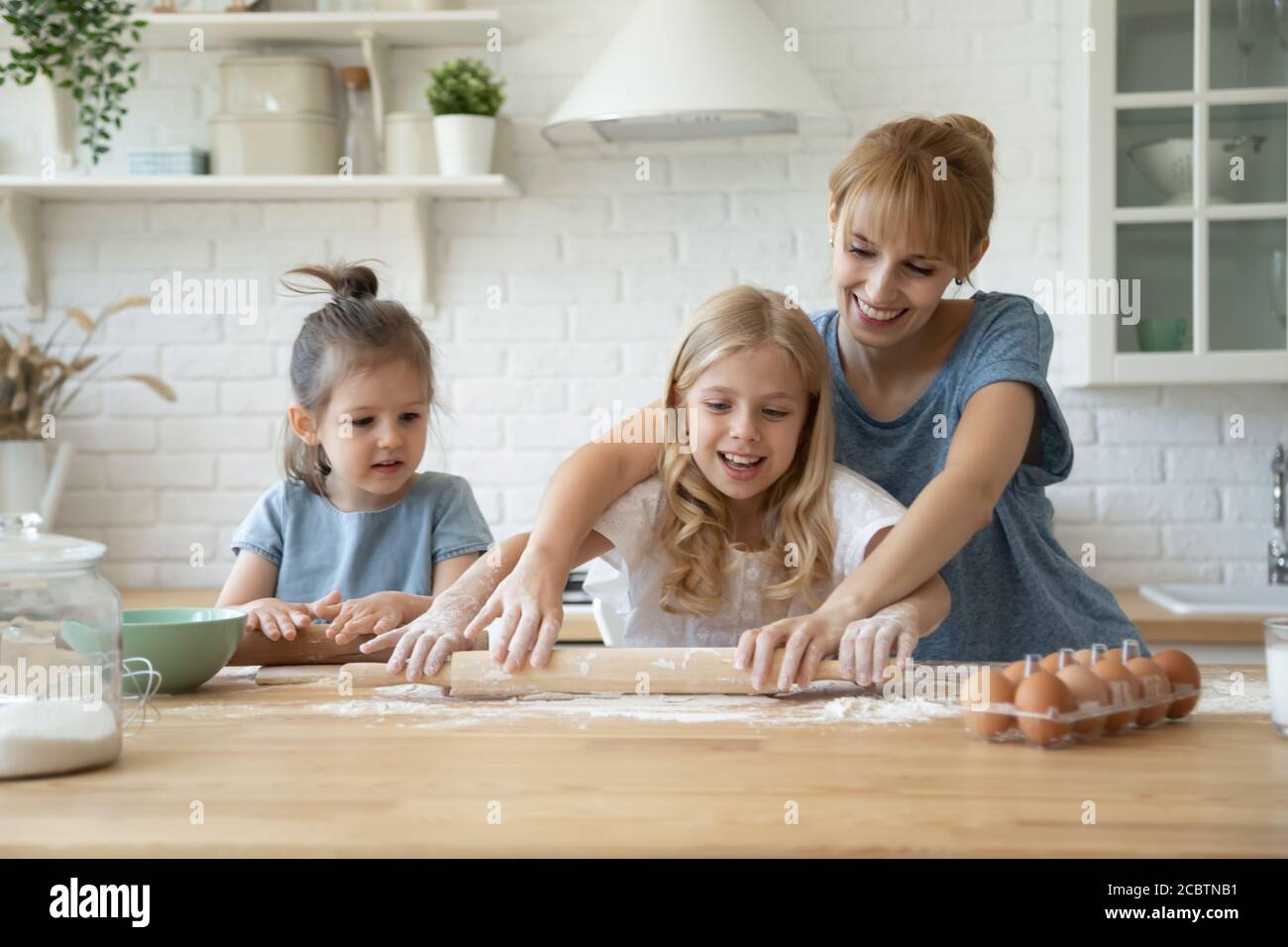 Millennial mother showing her little daughters how to roll dough Stock Photo
