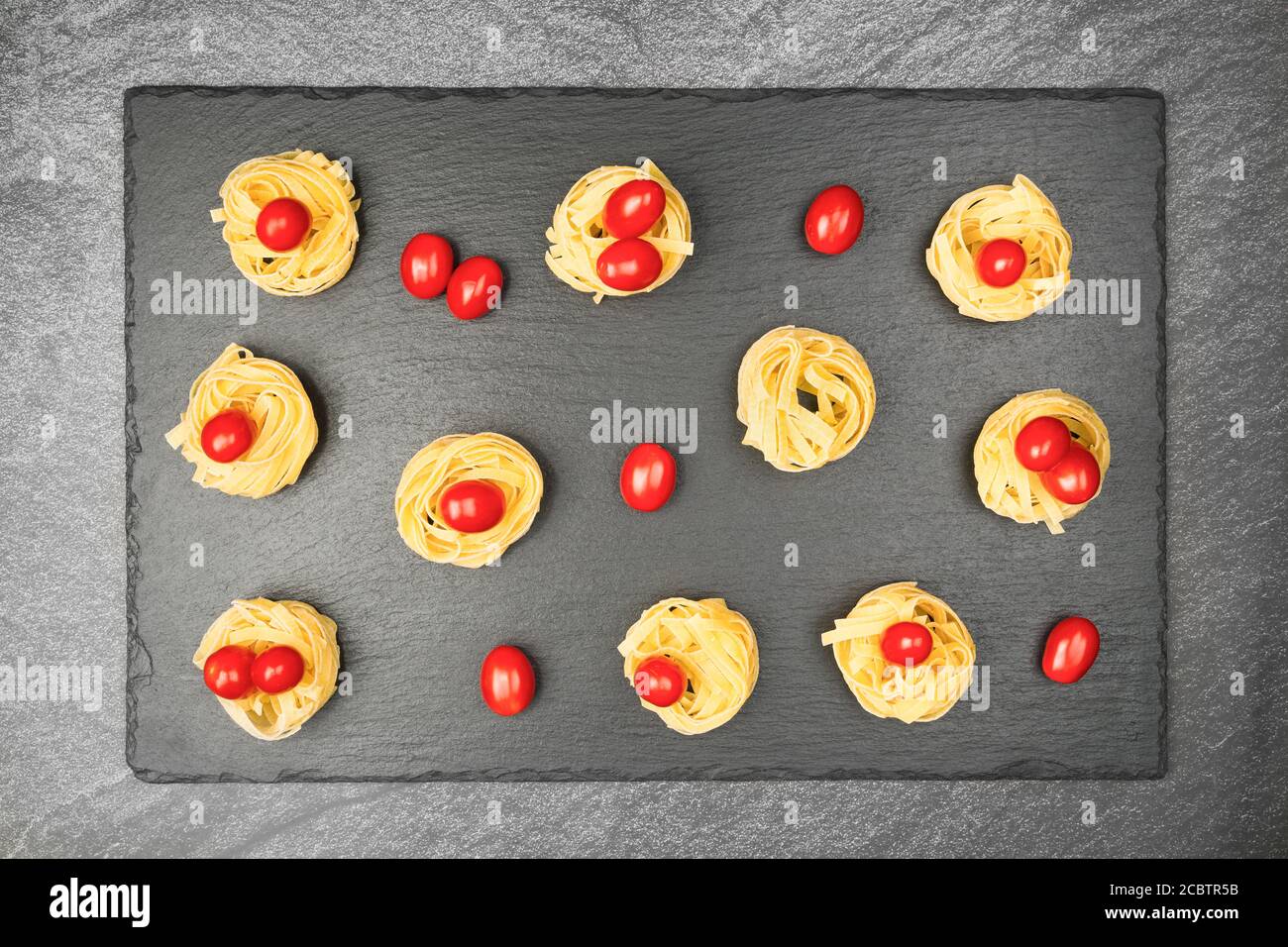 Close up of nests of tagliatelle noodles with egg-shaped mini roma tomatoes on a rustic wooden table wit burlap, Stock Photo