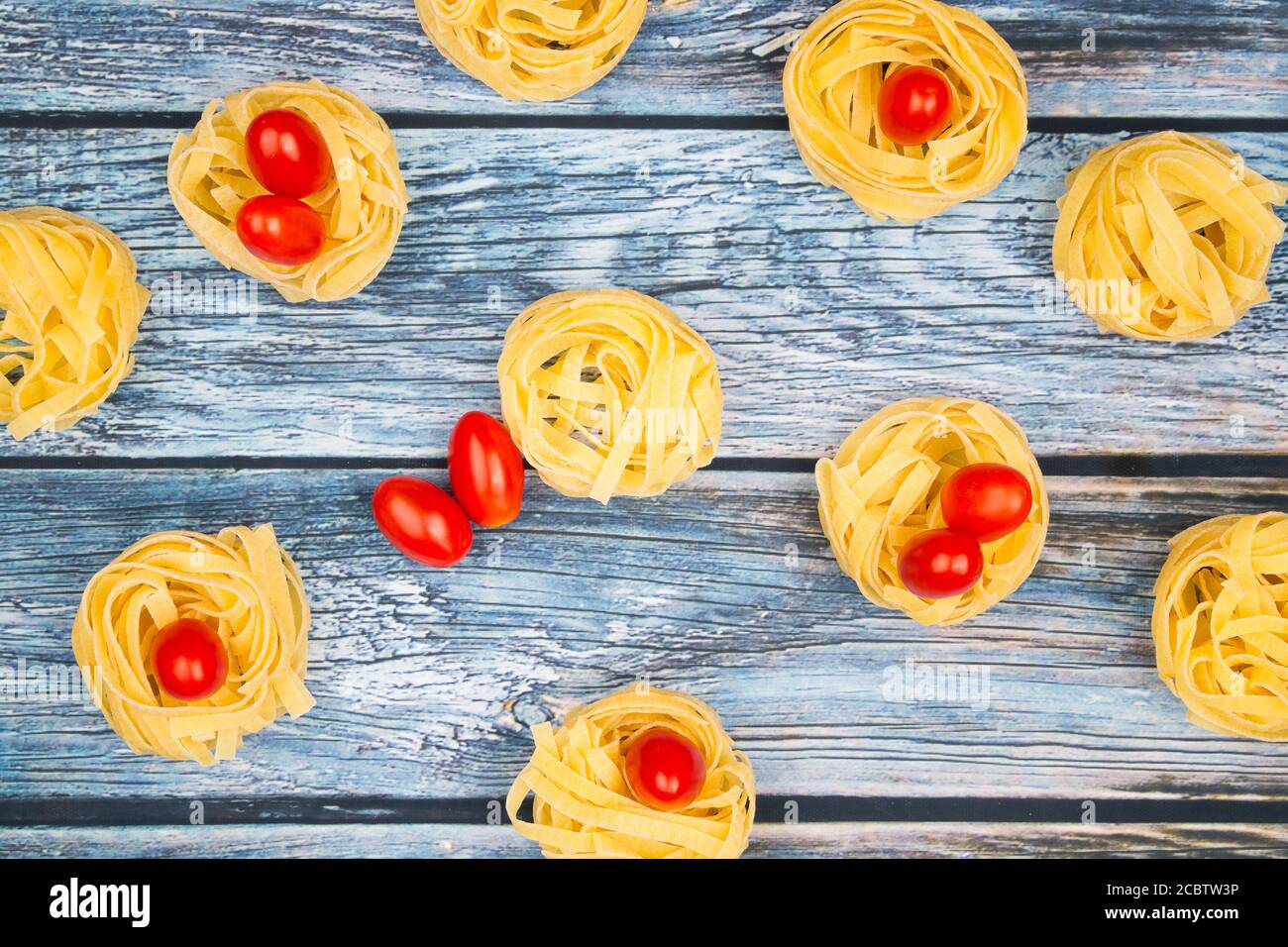 Close up of nests of tagliatelle noodles with egg-shaped mini roma tomatoes on a rustic wooden table wit burlap, Stock Photo