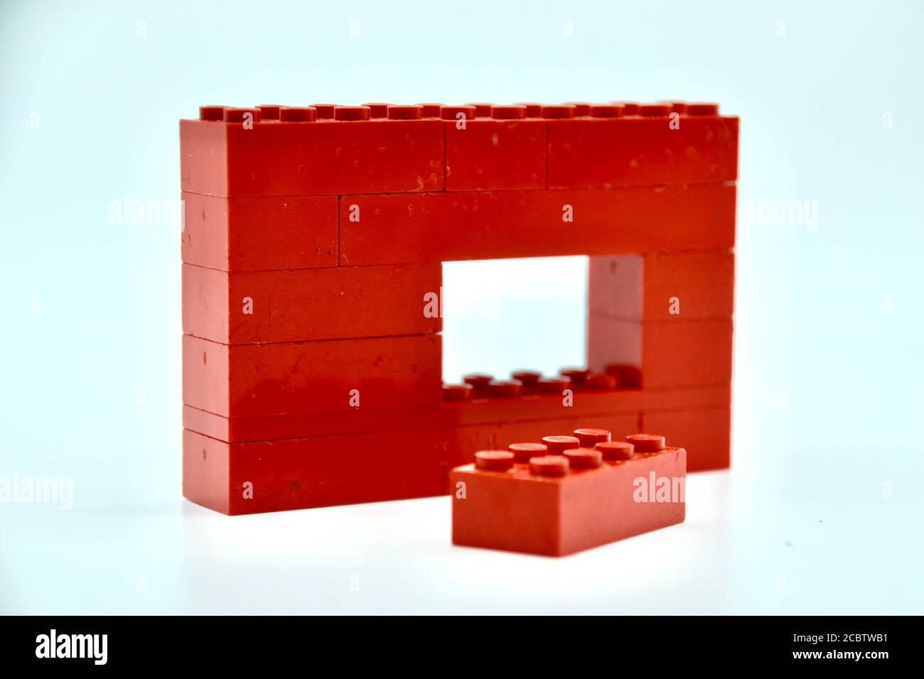 Concept studio image of a red Lego brick wall on white background with a gap in it and a single brick out front symbolizing individualism Stock Photo