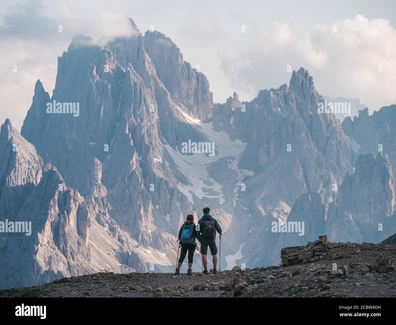 Couple of hikers standing and admiring stunning beauty of impressive jagged peaks of Cadini di misurina mountain group in Dolomites, Italy, part of Tr Stock Photo