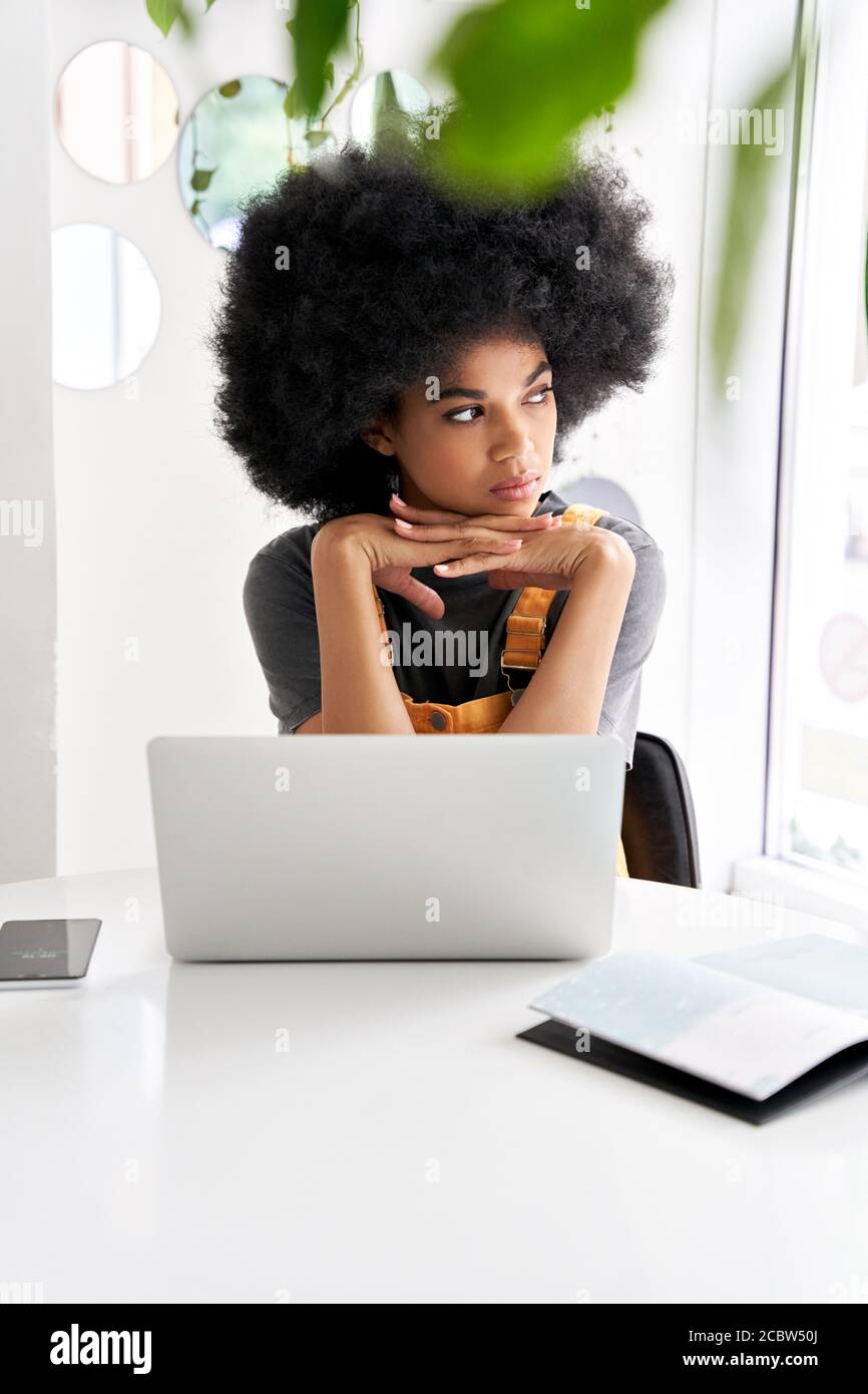 Thoughtful African girl looking through window sitting at cafe table use laptop. Stock Photo