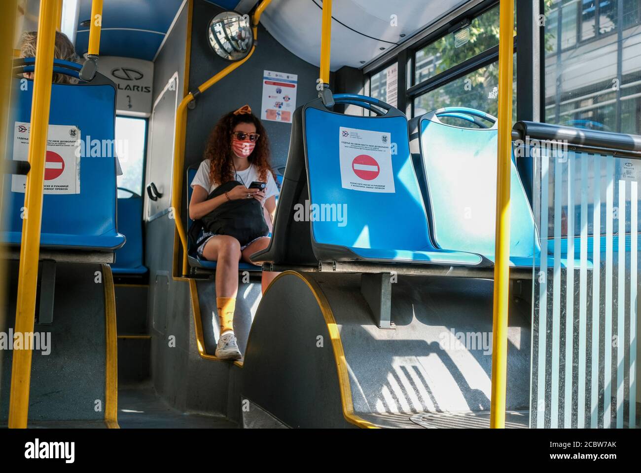Belgrade / Serbia - August 8, 2020: Young girl wearing a medical face mask on Belgrade city public bus with posters warning to keep social distance on Stock Photo