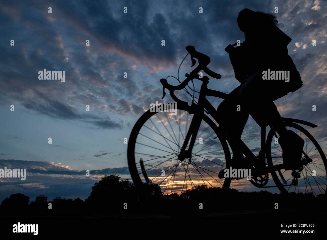 A cyclist rides with no hands on the handlebars through a London park at sunset Stock Photo
