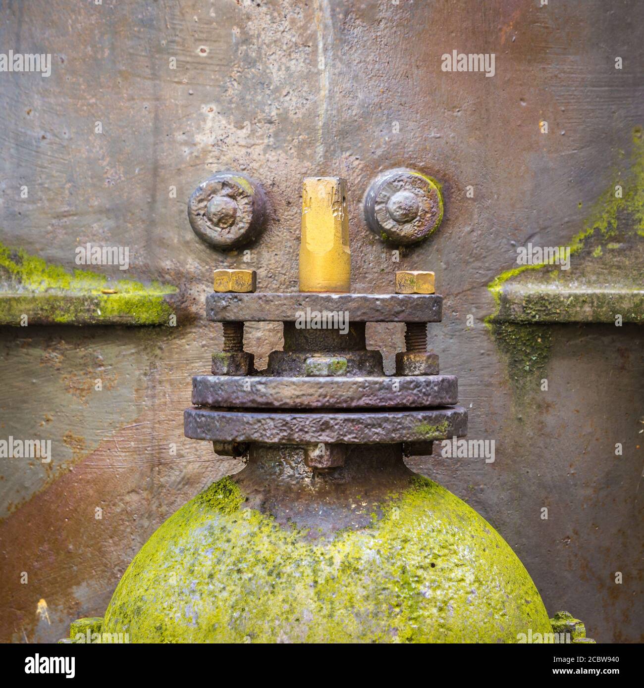 An old water tank with its rivets and valve looking like a funny robot ...