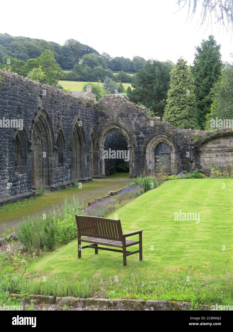 A garden bench overlooking the lawns & archways in the ancient stone walls of 14th century Whalley Abbey; a scenic place to visit, Ribble Valley. Stock Photo