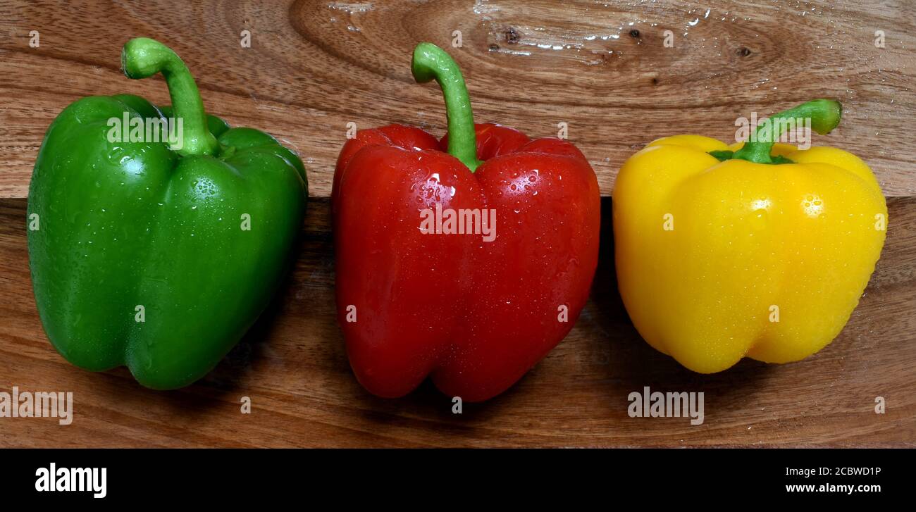 Peppers sweet bell, mixed Red, green yellow colors, fresh washed, wet, closeup, perfect skin, enticing image viewed from above on wooden chop board. Stock Photo