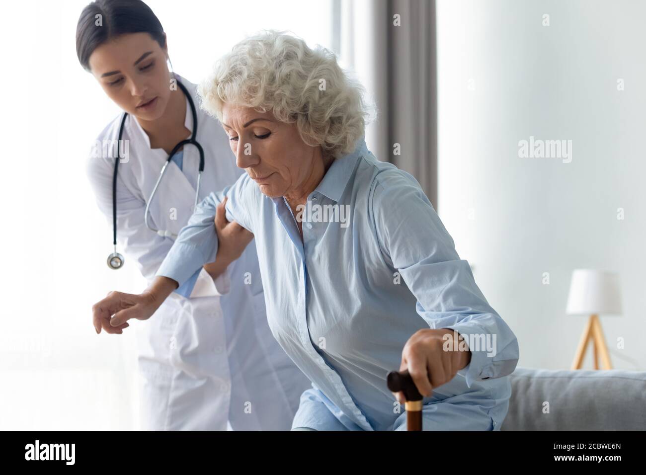 Careful young female physiotherapist helping older senior disabled patient. Stock Photo