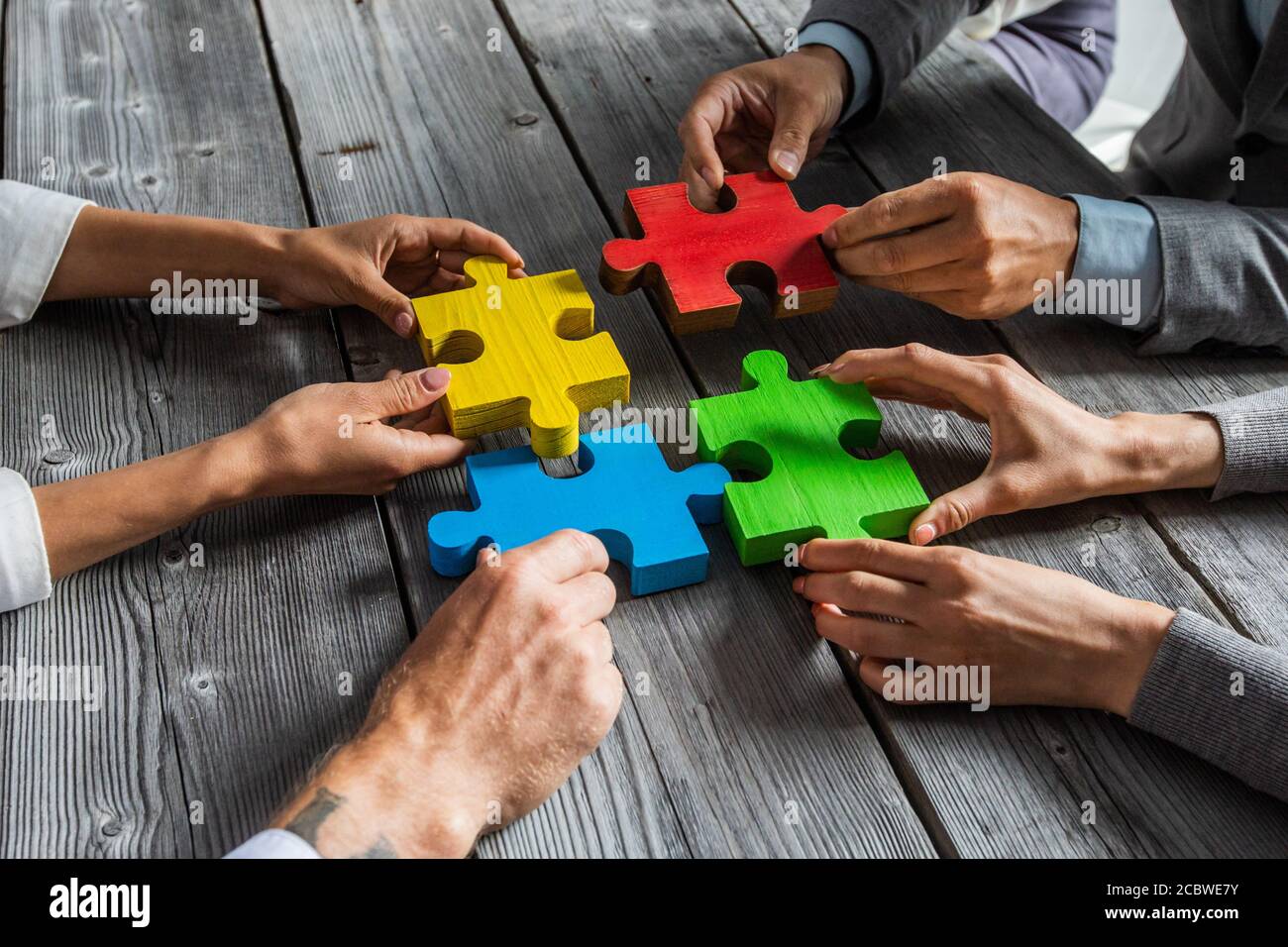 Business people team sitting around meeting table and assembling color jigsaw  puzzle pieces unity cooperation ideas concept Stock Photo - Alamy