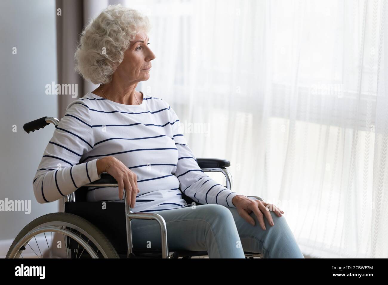 Thoughtful middle aged old hoary woman sitting in wheelchair. Stock Photo