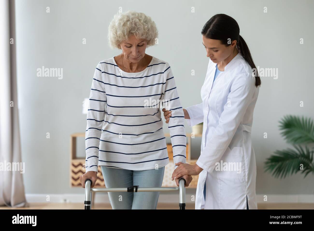 Medical worker helping older mature disabled woman walking with frame ...