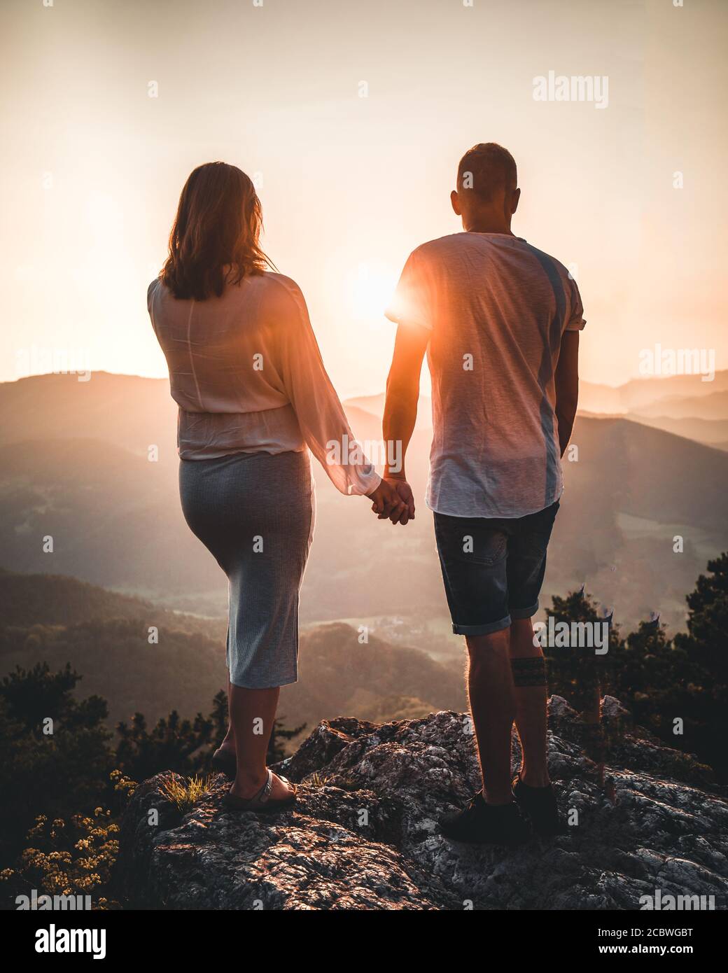 Happy couple holding hands on the mountain top during sunset - rear ...