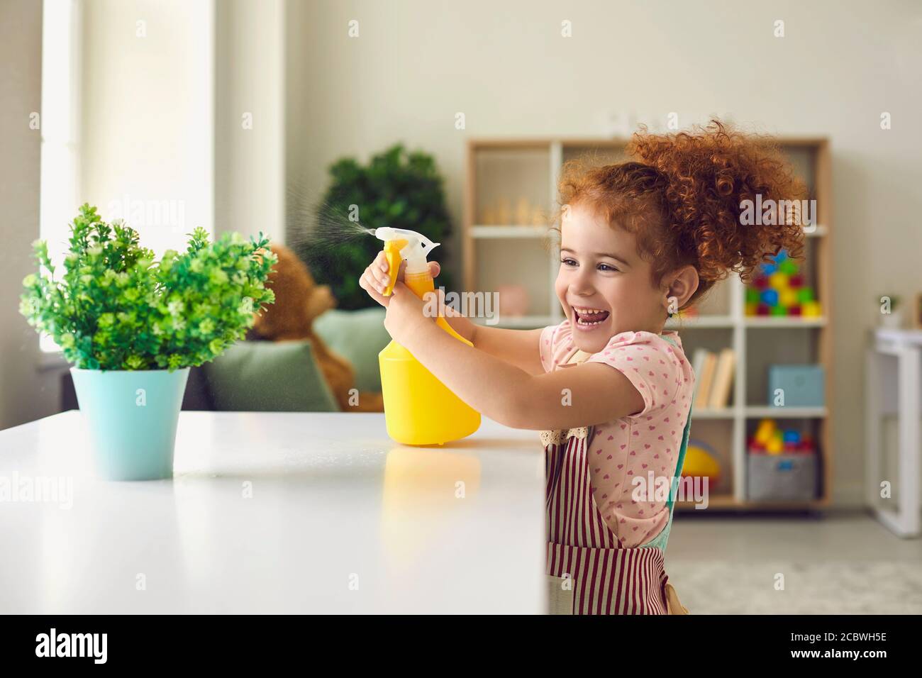 Little girl spraying water on houseplant at home. Cute child helping