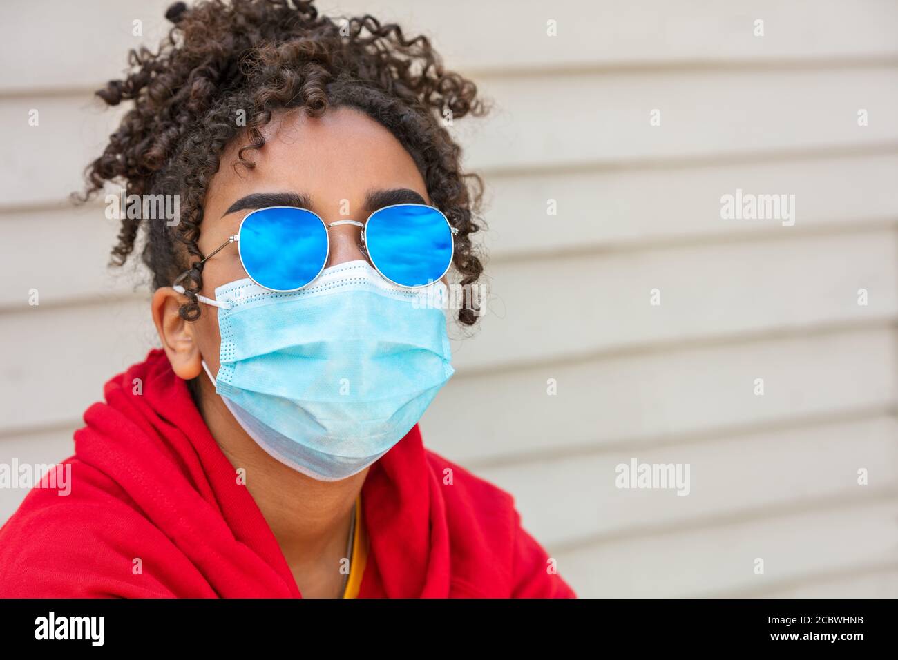 Girl teenager teen mixed race biracial African American female young woman wearing blue sunglasses and face mask in Coronavirus COVID-19 pandemic Stock Photo