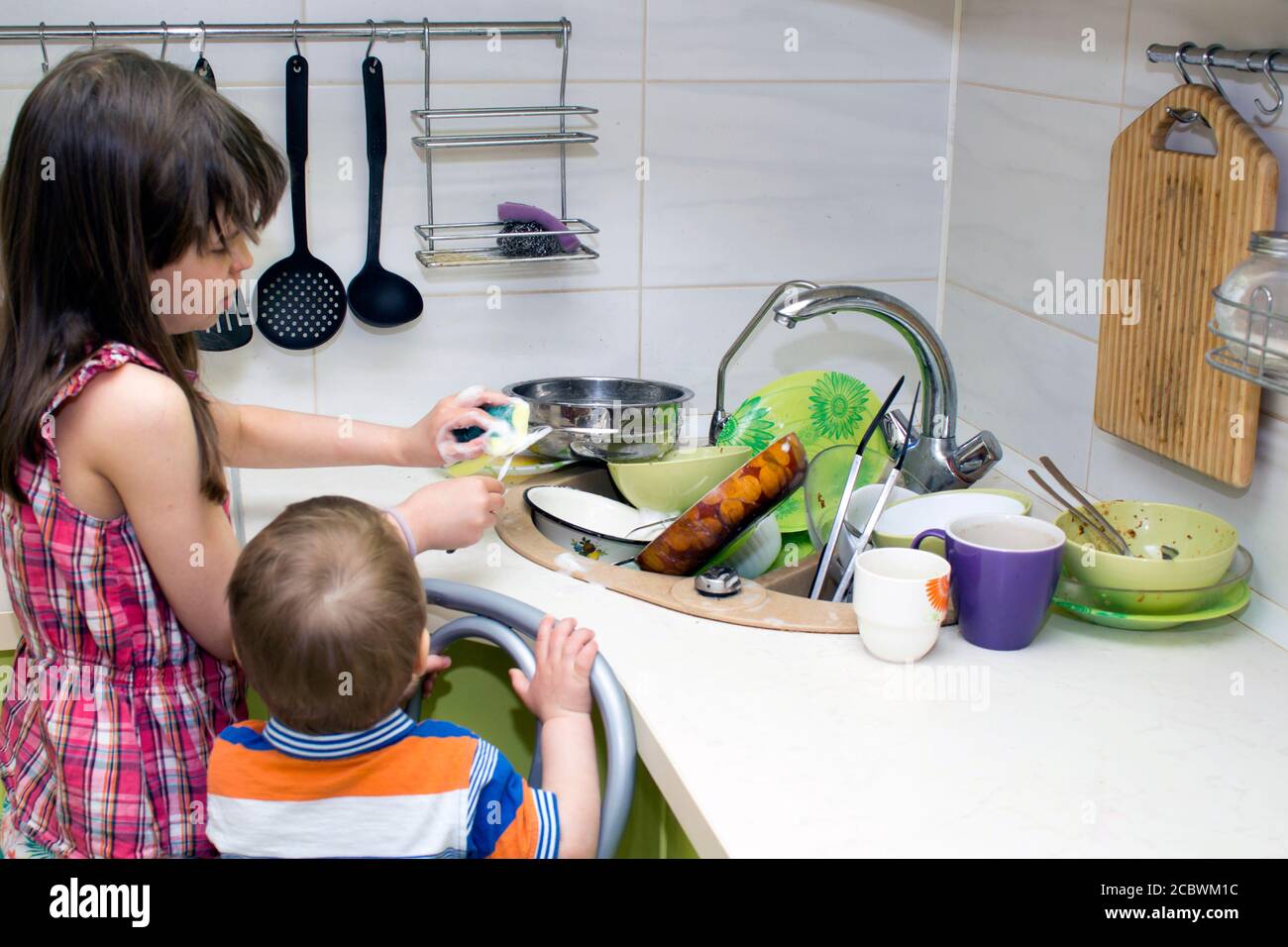 The child washes a bunch of dirty dishes standing near the sink Stock ...