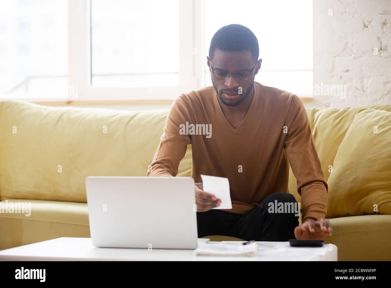 Unhappy african american man reviewing financial bill at home Stock Photo