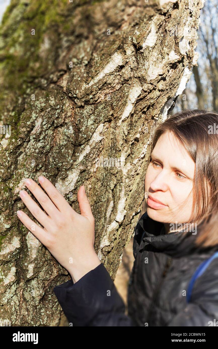 Girl hugging a huge tree trunk in the Park, smiling at the camera. The concept of protection of nature Stock Photo