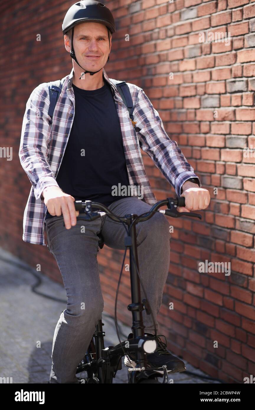 Mature Caucasian man in a bicycle helmet on his bike in a city against red brick wall Stock Photo